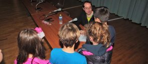 aris dimokidis sits on a wooden table and speaks to 4 students of mandoulides schools