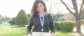 Student Ch. Patsia wearing her medal and holding her award, with green and trees at the background