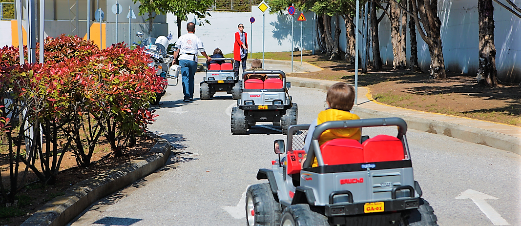 Three small toy cars driven by students of Mandoulides schools beatles, move on a road, while two teachers teach them the correct way of driving